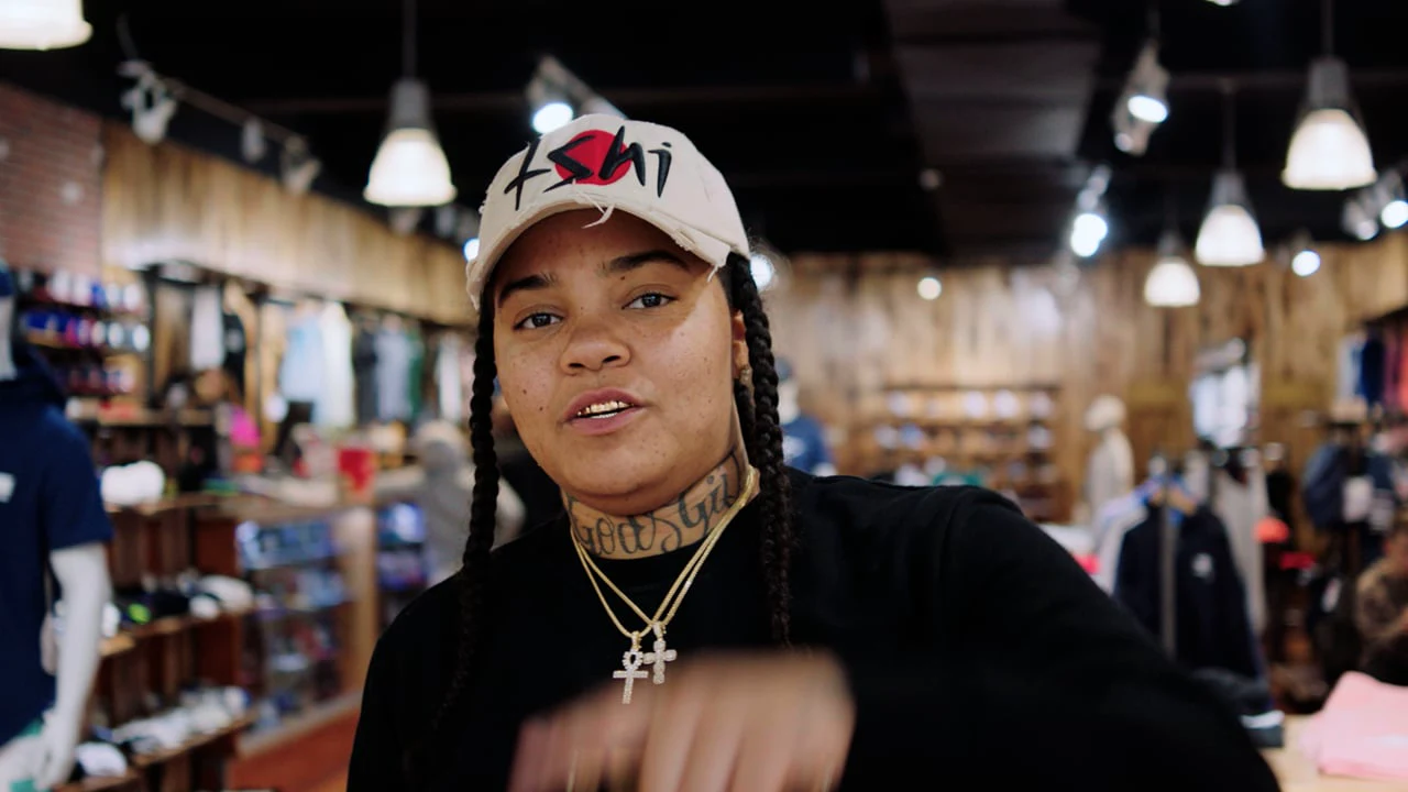 Young M.A wearing a white cap and black shirt inside a clothing store